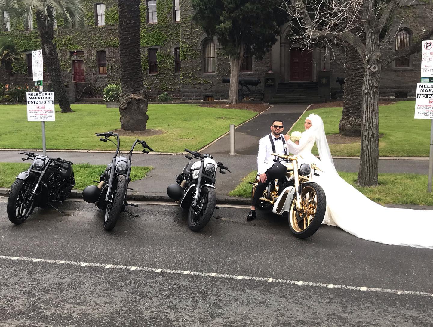 Bride and groom on a gold Harley beside black Harleys outside a heritage building