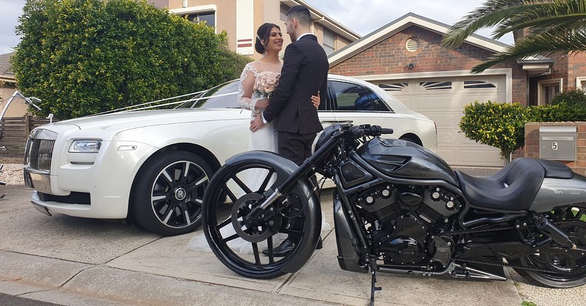 Bride and groom beside a black Harley and a white wedding car