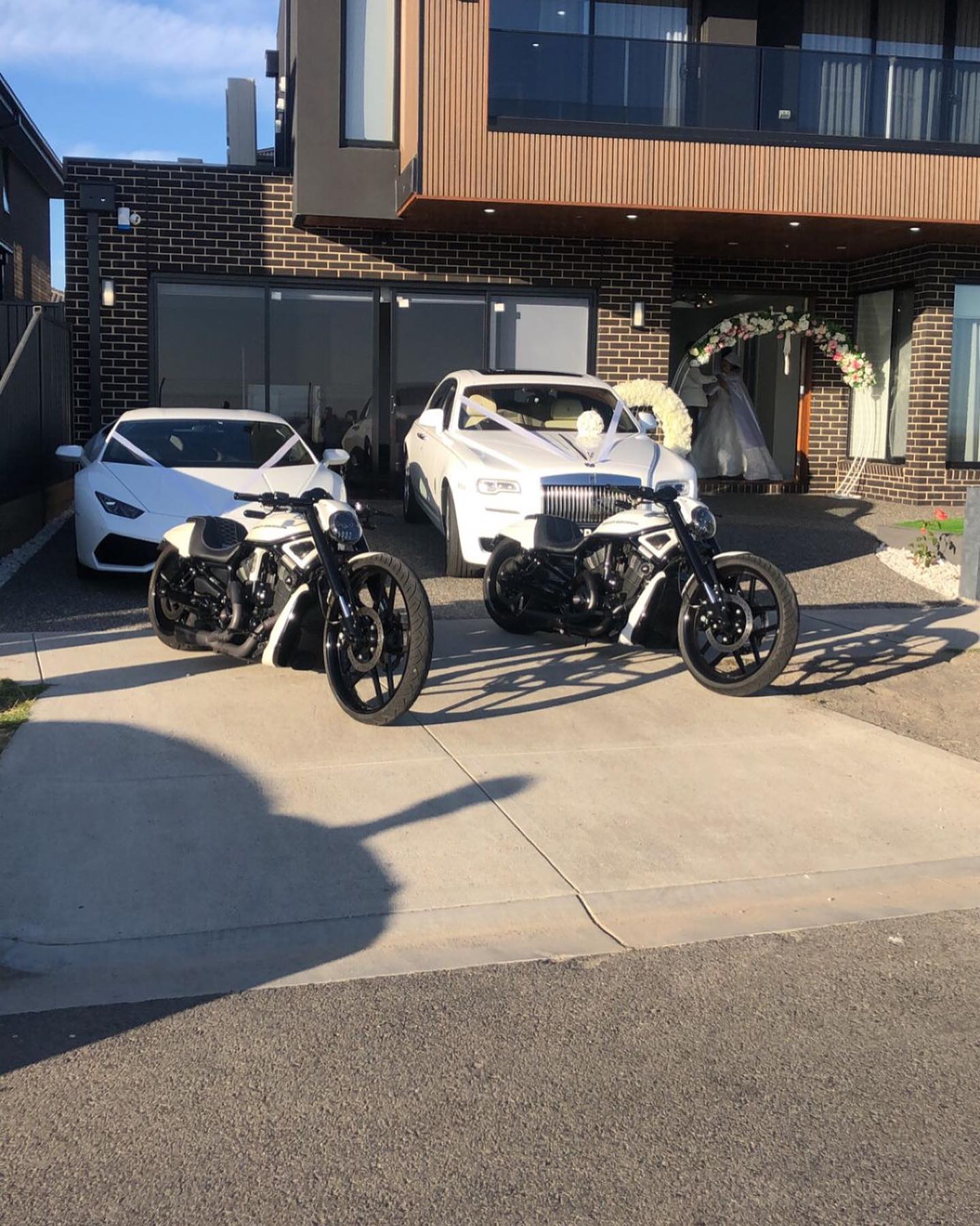 Two black and white Harleys parked in a driveway in front of white wedding cars
