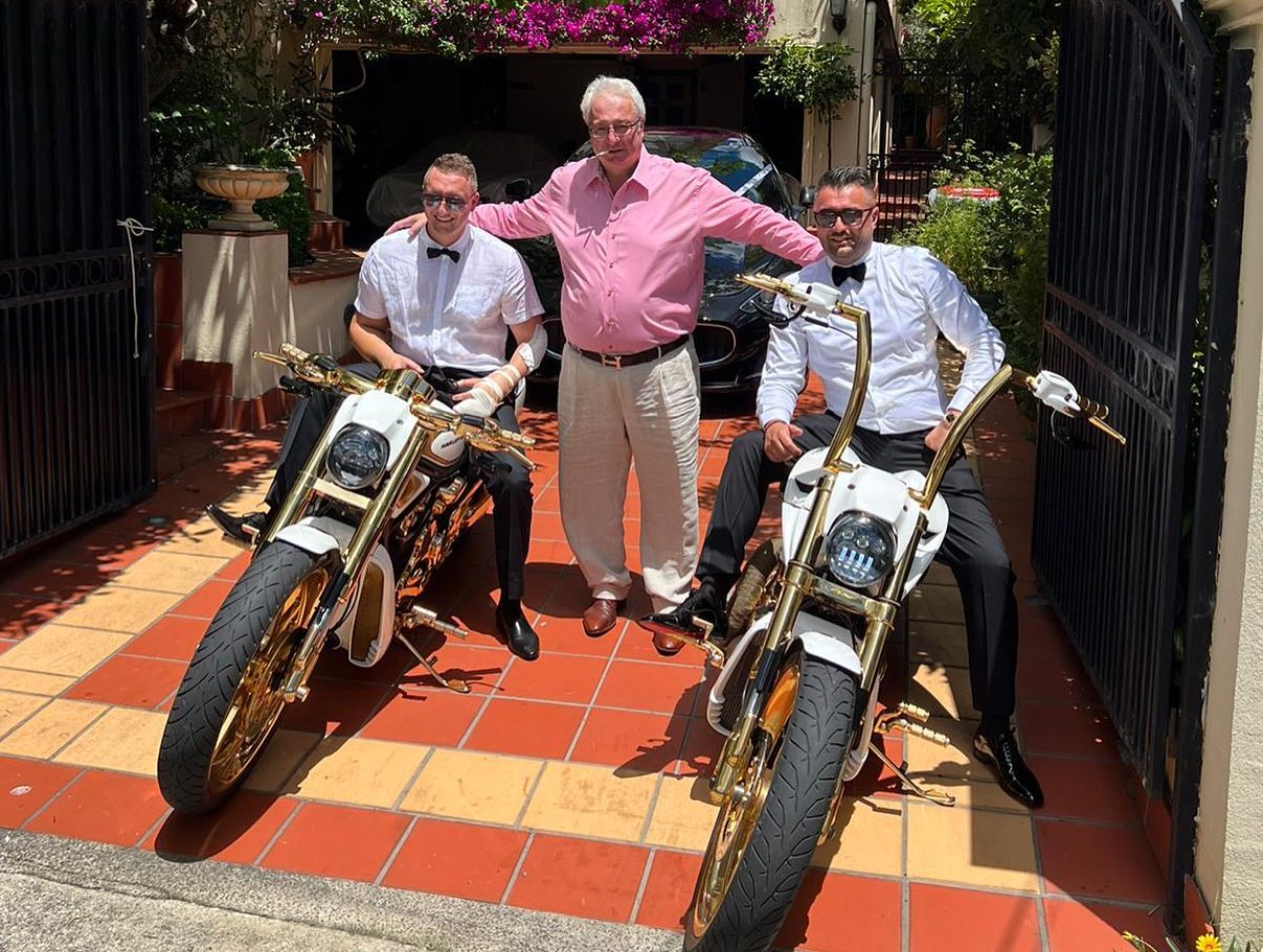 Two men in bow ties seated on gold-trimmed Harleys with an older man between them