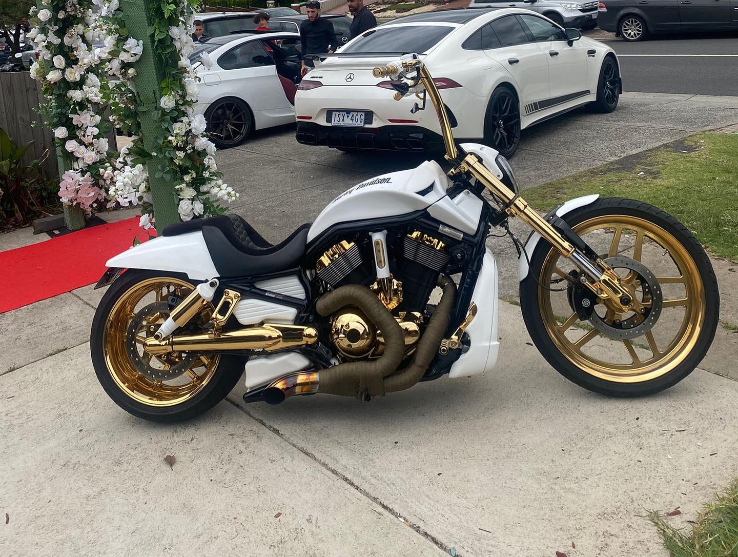 White Harley with gold wheels and frame parked beside a floral arch