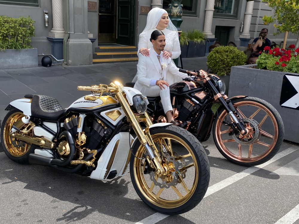 Bride and groom seated on gold and copper Harleys outside a heritage building
