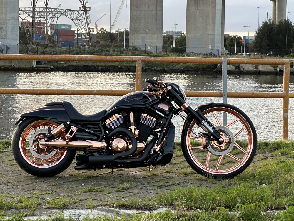 Black Harley with copper wheels parked on grass beside a river
