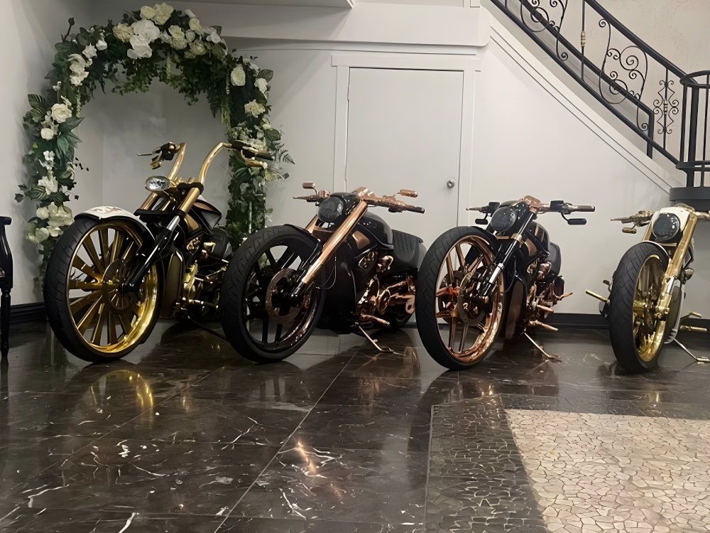 Four gold and copper custom Harleys lined up beside a floral arch indoors