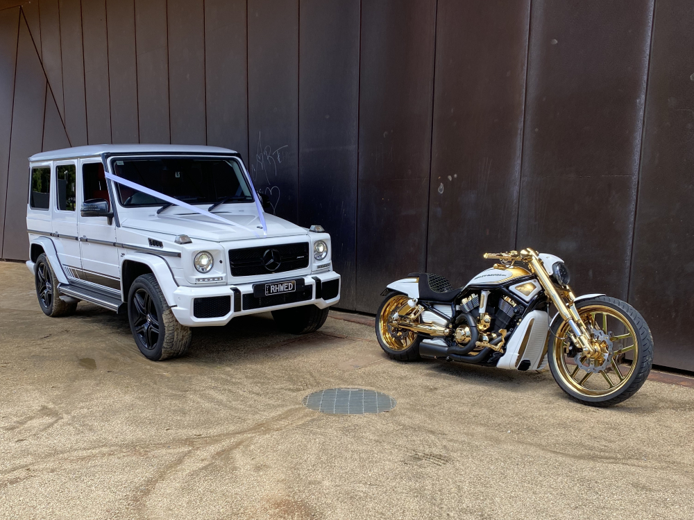 Gold-trimmed white Harley parked beside a white four-wheel drive with wedding ribbons