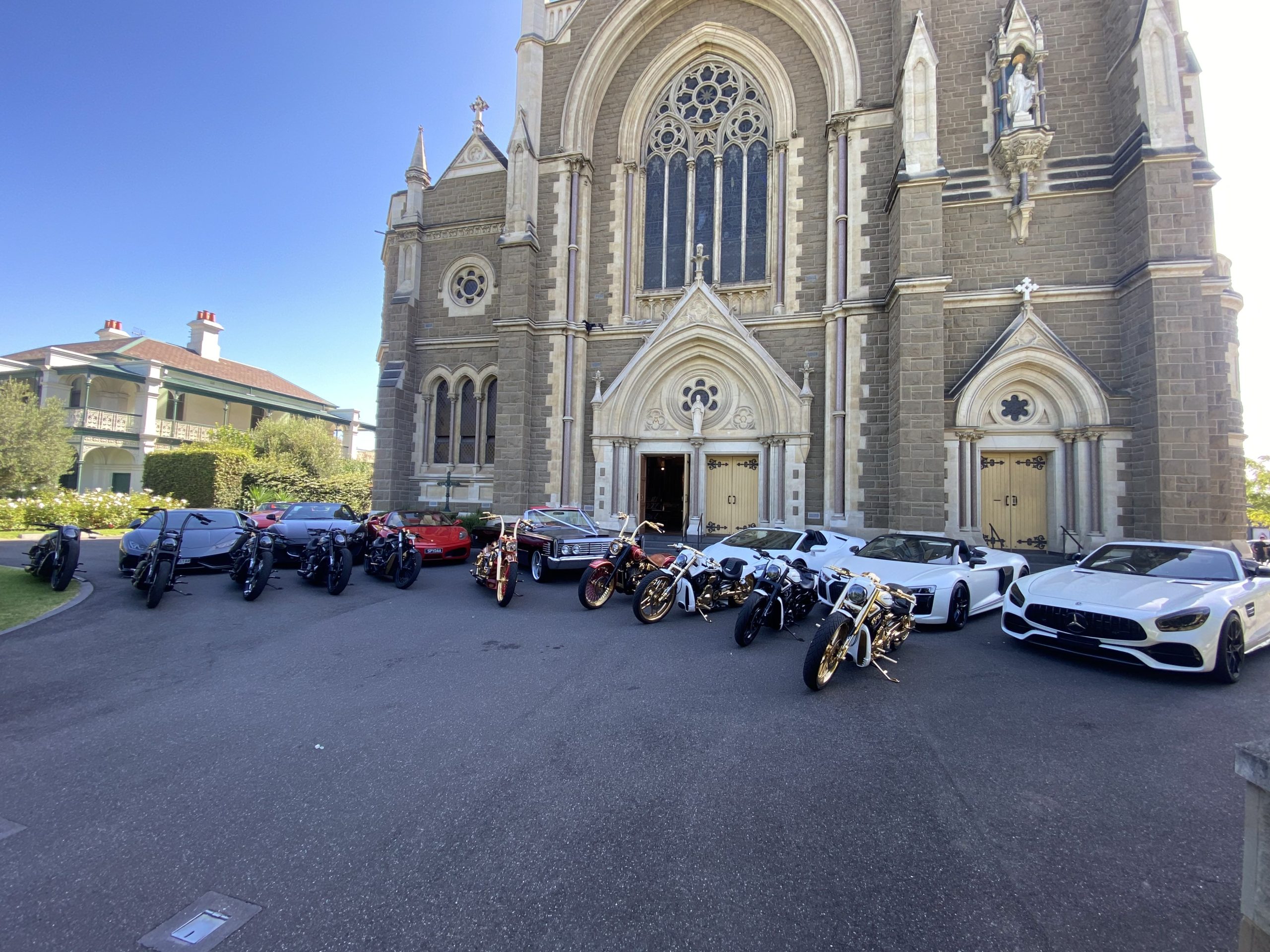 Harleys and white luxury cars lined up in front of a grey stone church