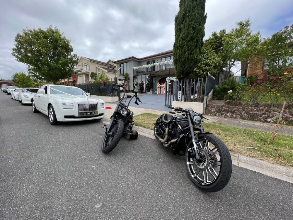 Two black Harleys parked in a street ahead of a line of white wedding cars