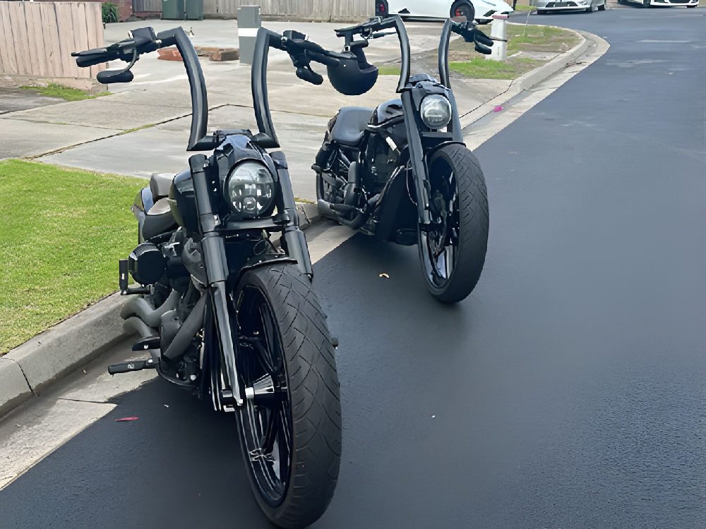 Two black Harleys with tall ape-hanger handlebars parked at the kerb