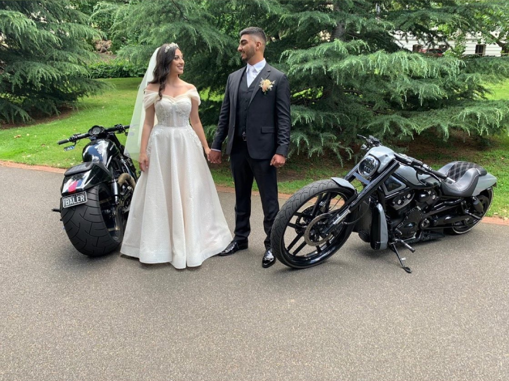 Bride and groom holding hands between two black Harleys