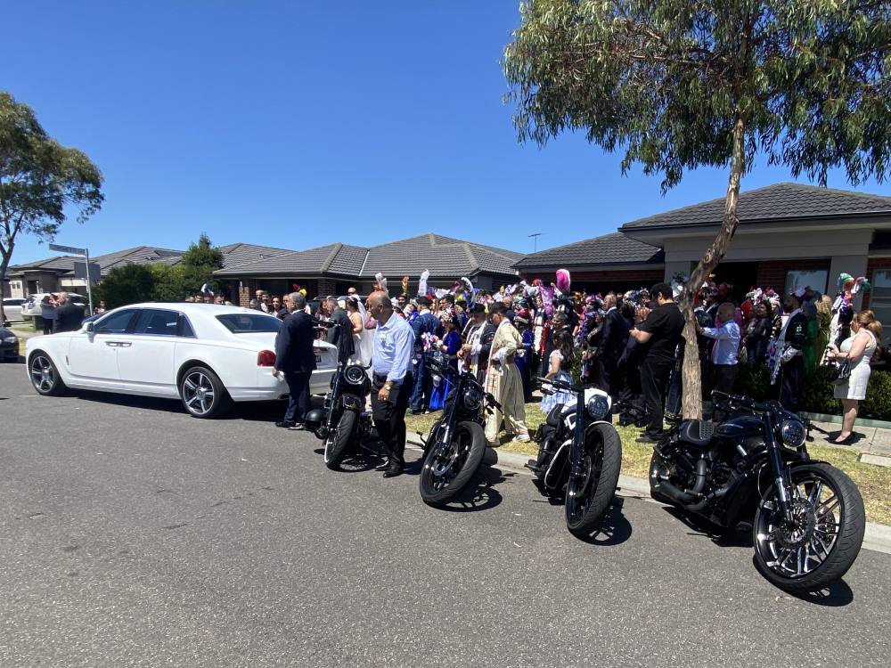 Row of black Harleys and a white luxury car in front of a crowd of guests