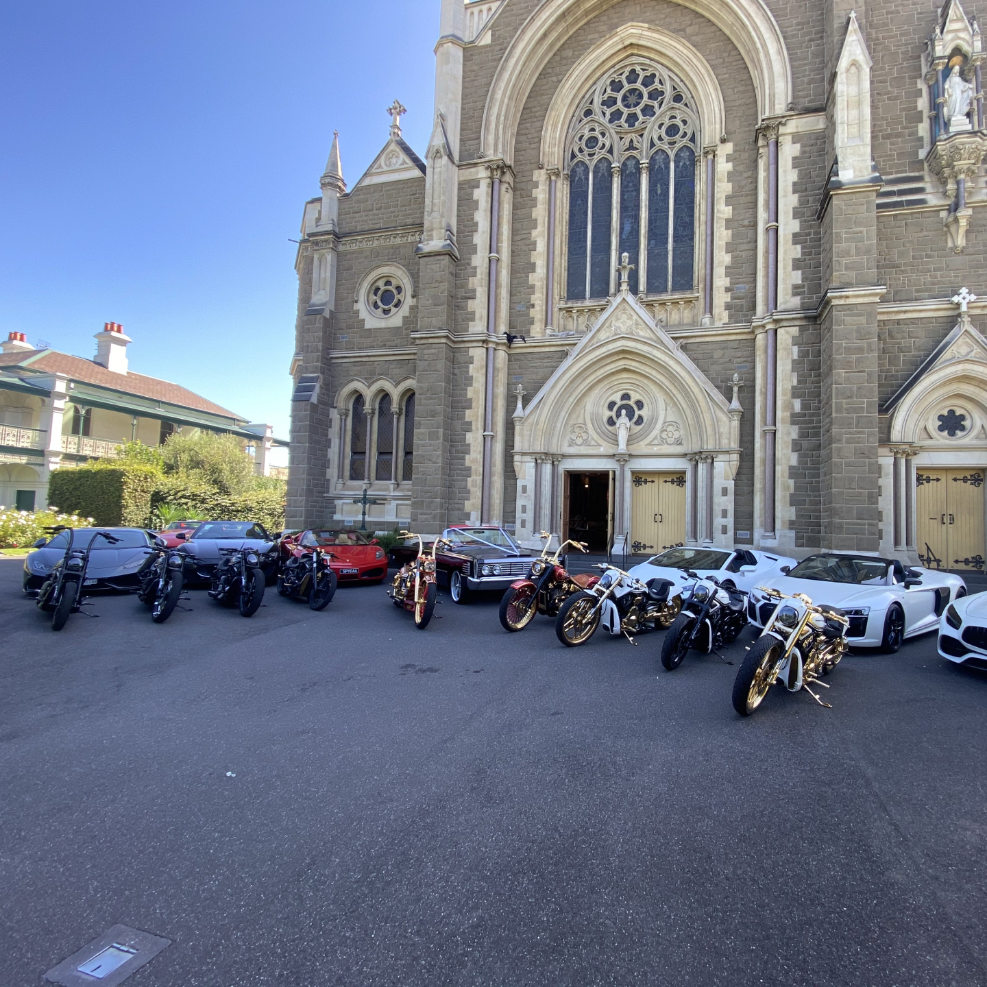 Harleys and luxury cars parked in front of a grey stone church